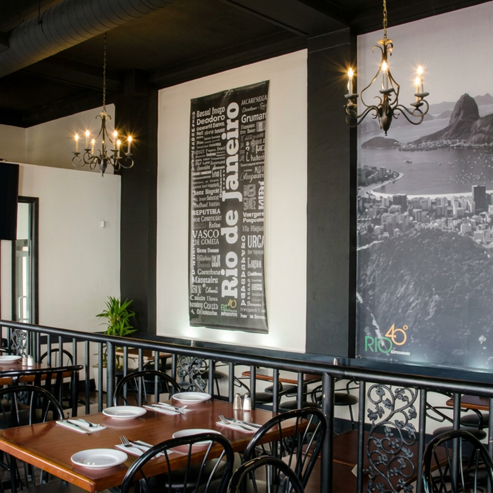 Brazilian restaurant dining room with set tables, black railings, chandeliers, and large Rio de Janeiro artwork.